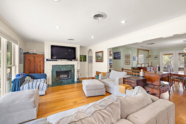 living room featuring visible vents, a premium fireplace, crown molding, light wood-type flooring, and recessed lighting