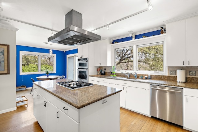 kitchen featuring island exhaust hood, appliances with stainless steel finishes, white cabinets, a sink, and a kitchen island