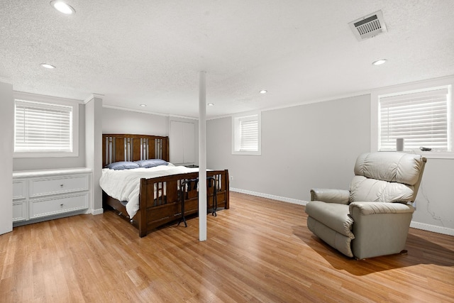 bedroom featuring baseboards, visible vents, a textured ceiling, light wood-style floors, and multiple windows