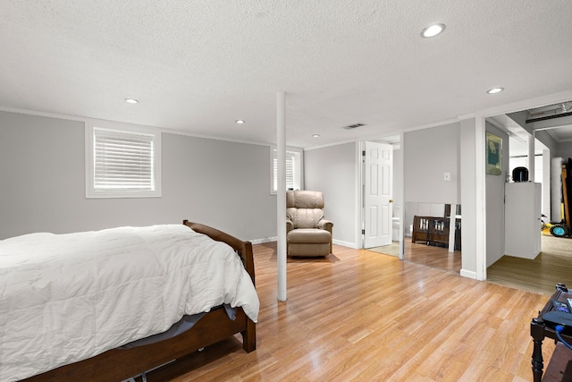 bedroom with a textured ceiling, recessed lighting, visible vents, ornamental molding, and light wood finished floors