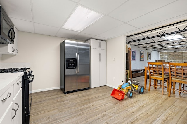 kitchen with a drop ceiling, light wood-style flooring, white cabinets, light countertops, and black appliances