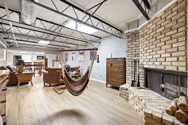 living room featuring a brick fireplace, a textured wall, baseboards, and wood finished floors