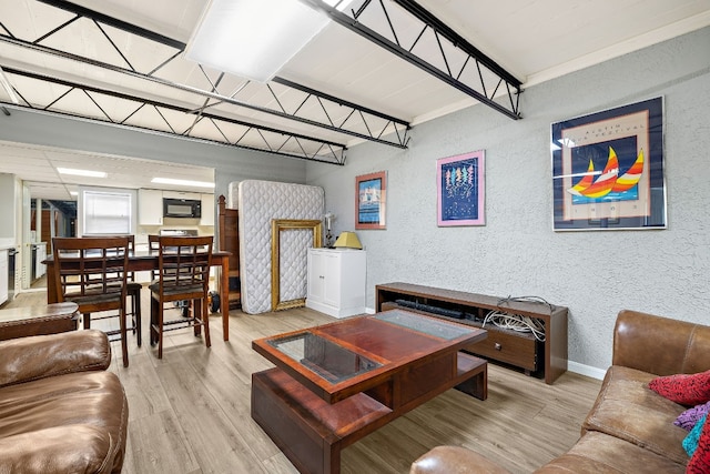 living area with a textured wall, light wood-type flooring, and baseboards