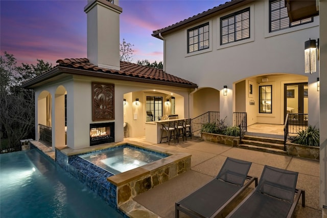 back of house featuring a patio, a chimney, an outdoor bar, an in ground hot tub, and a multi sided fireplace