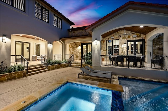 pool at dusk with french doors, a patio area, an outdoor pool, and an in ground hot tub