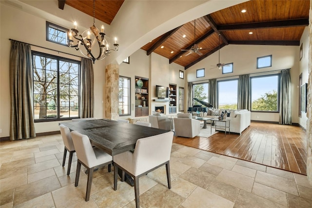 dining room with high vaulted ceiling, wooden ceiling, a lit fireplace, and baseboards