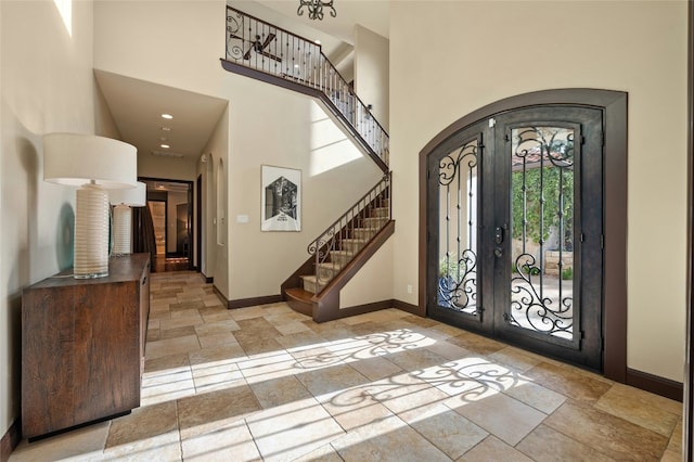 foyer entrance featuring stone tile floors, arched walkways, baseboards, a towering ceiling, and stairs