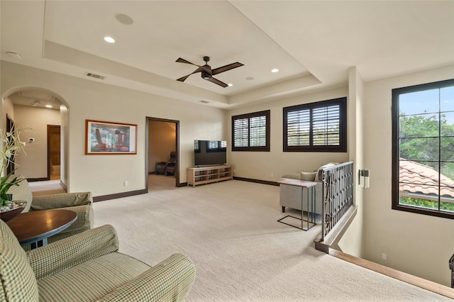 living room with arched walkways, a raised ceiling, light colored carpet, and baseboards