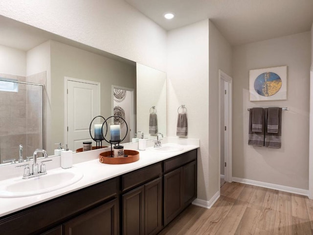 bathroom featuring double vanity, wood finished floors, a sink, and a shower stall