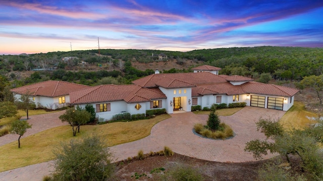 mediterranean / spanish-style house featuring an attached garage, a tile roof, decorative driveway, and a yard