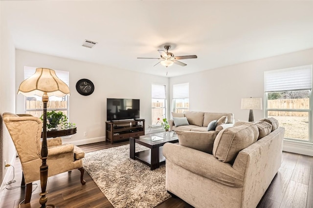 living area featuring a healthy amount of sunlight, baseboards, dark wood finished floors, and a ceiling fan