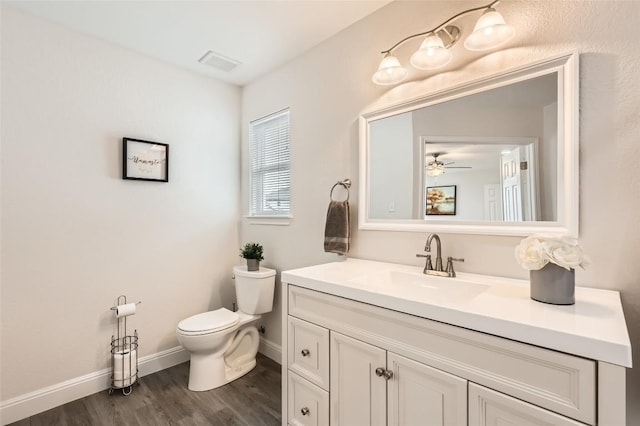 half bath with visible vents, toilet, vanity, wood finished floors, and baseboards