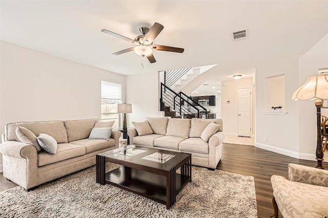 living area with visible vents, baseboards, dark wood finished floors, a ceiling fan, and stairs