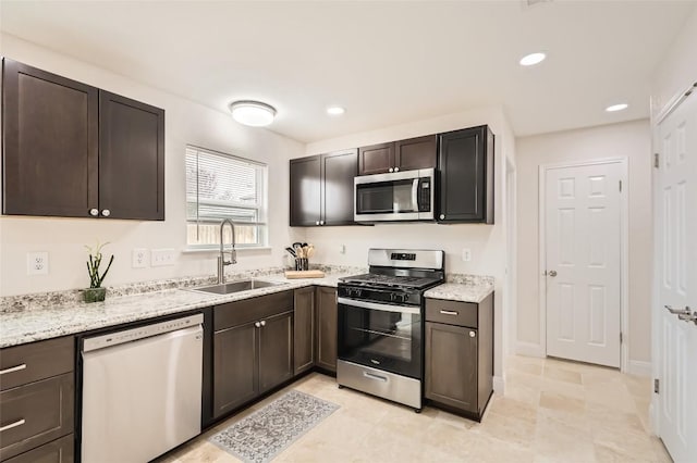 kitchen with light stone counters, appliances with stainless steel finishes, dark brown cabinets, a sink, and recessed lighting