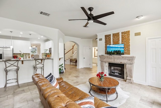 living area with arched walkways, crown molding, a fireplace, visible vents, and a ceiling fan