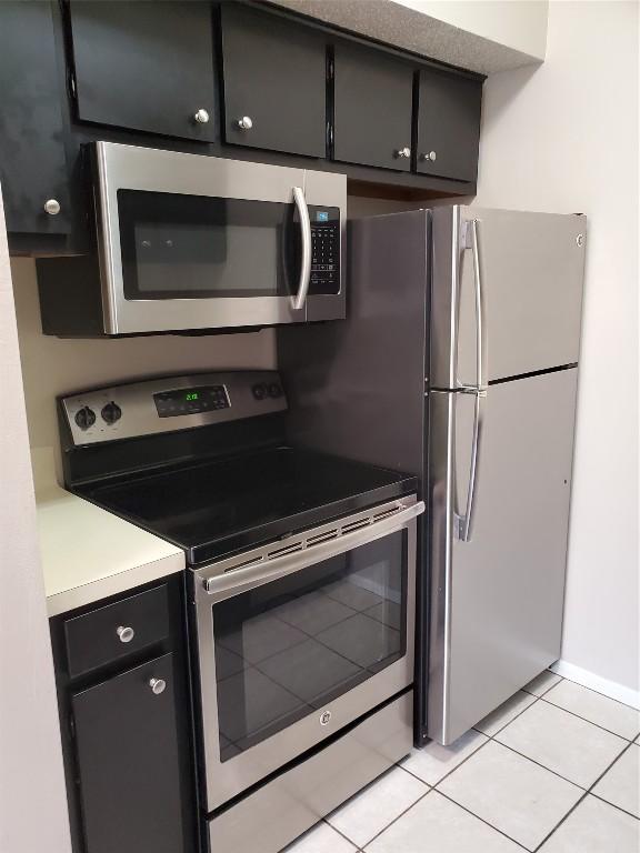 kitchen featuring appliances with stainless steel finishes, light countertops, dark cabinetry, and light tile patterned flooring