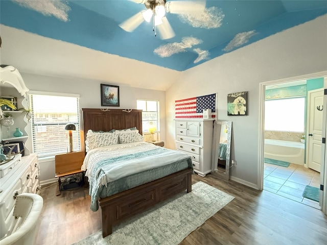 bedroom featuring ceiling fan, vaulted ceiling, ensuite bath, wood finished floors, and baseboards