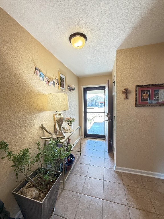 doorway featuring a textured ceiling, a textured wall, light tile patterned floors, and baseboards