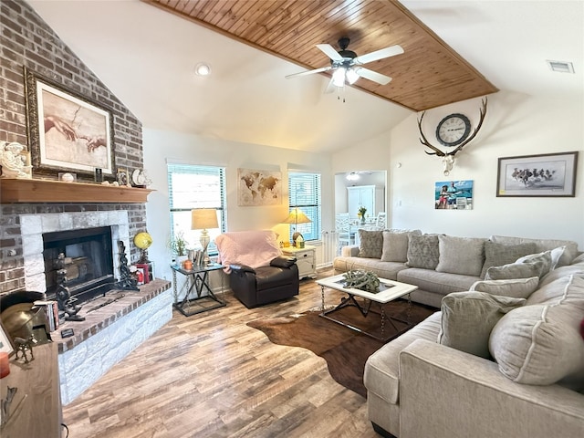 living area with a brick fireplace, visible vents, ceiling fan, vaulted ceiling, and light wood-style floors