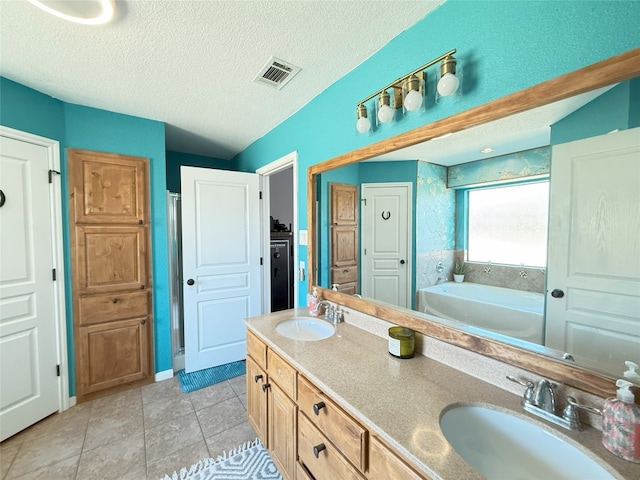 bathroom with a garden tub, a textured ceiling, a sink, and visible vents