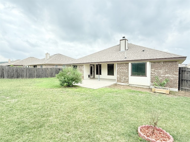 back of property with a patio, a fenced backyard, a chimney, brick siding, and a yard