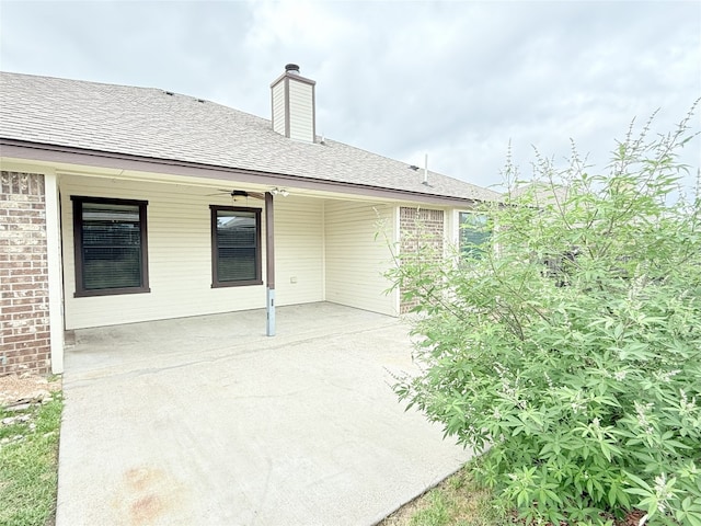 back of property featuring a patio, brick siding, roof with shingles, and a chimney