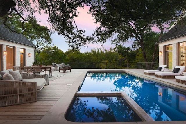 pool at dusk featuring an outdoor hangout area, outdoor dining area, a pool with connected hot tub, and a wooden deck