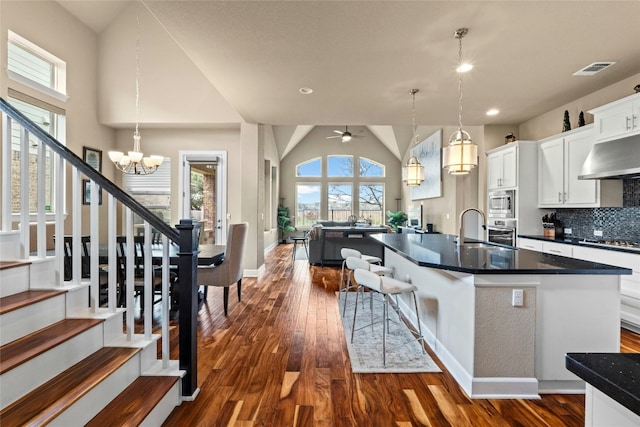 kitchen with dark wood-type flooring, white cabinetry, a center island with sink, and pendant lighting