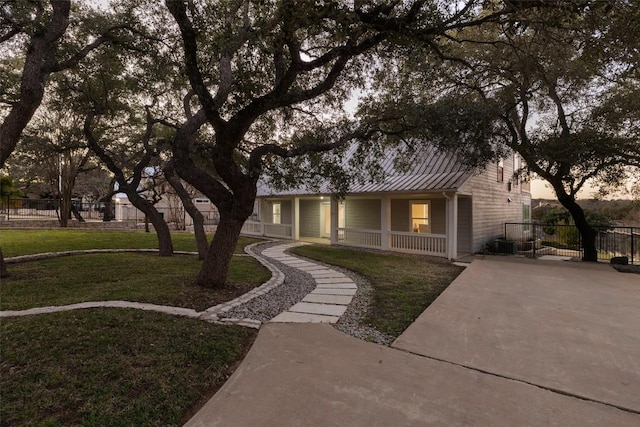 view of property hidden behind natural elements featuring a standing seam roof, fence, a front lawn, and metal roof