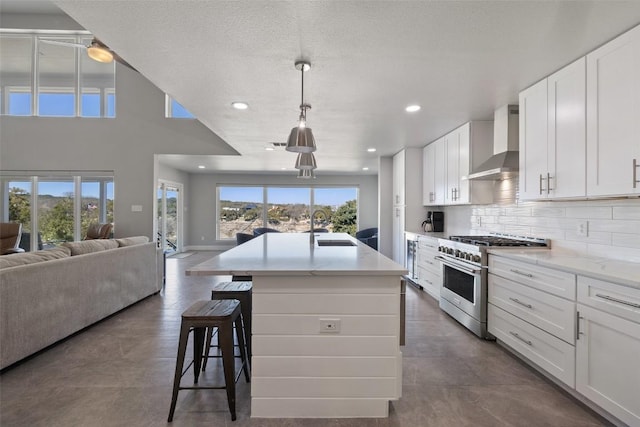 kitchen featuring stainless steel range, white cabinets, open floor plan, wall chimney range hood, and a sink