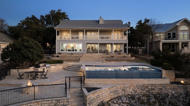 back of property at dusk with metal roof, an outdoor fire pit, a patio area, and a balcony