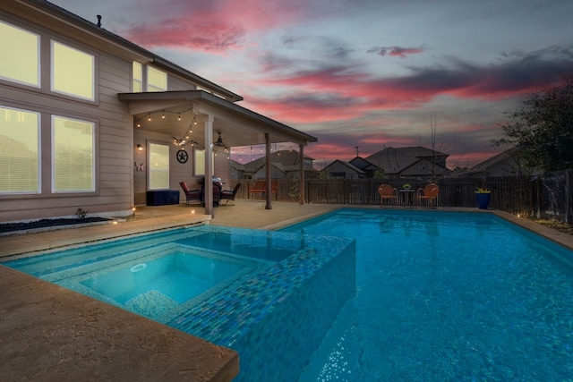 pool at dusk featuring a fenced backyard, ceiling fan, a patio area, and a pool with connected hot tub