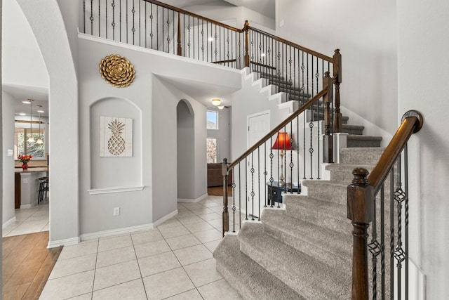 tiled foyer featuring arched walkways, stairway, a towering ceiling, and baseboards