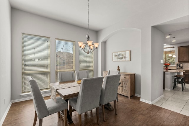 dining room featuring baseboards, a notable chandelier, light wood-style flooring, and arched walkways