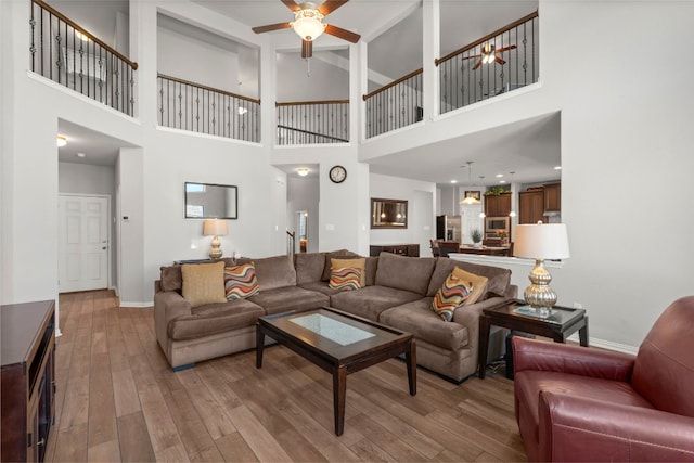 living room with baseboards, wood finished floors, a ceiling fan, and a high ceiling