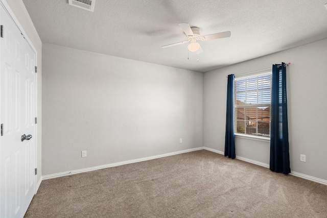 carpeted empty room with ceiling fan, a textured ceiling, baseboards, and visible vents