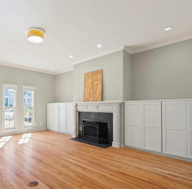 unfurnished living room featuring light wood finished floors, a fireplace with flush hearth, crown molding, and recessed lighting