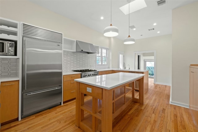 kitchen featuring wall chimney exhaust hood, stainless steel appliances, light countertops, and decorative light fixtures