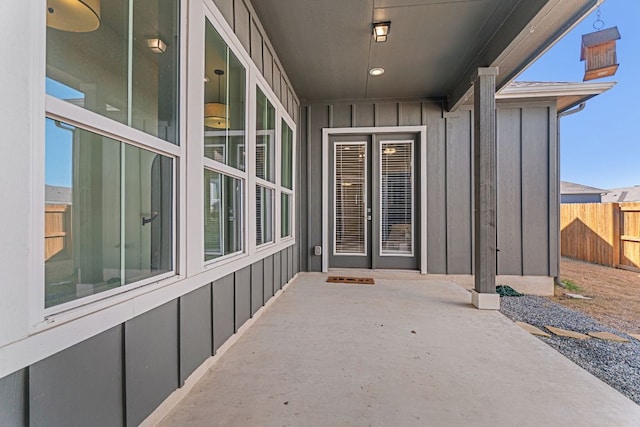 view of exterior entry with board and batten siding, a patio area, and fence