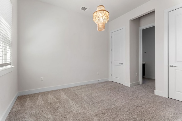 unfurnished room with light colored carpet, visible vents, a notable chandelier, and baseboards