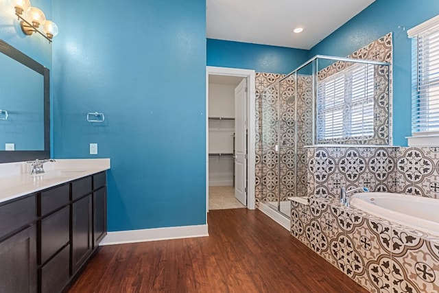 bathroom featuring a garden tub, wood finished floors, baseboards, a shower stall, and a walk in closet