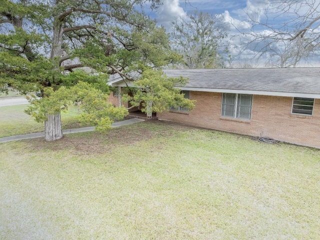 view of front of house with a shingled roof, a front yard, and brick siding