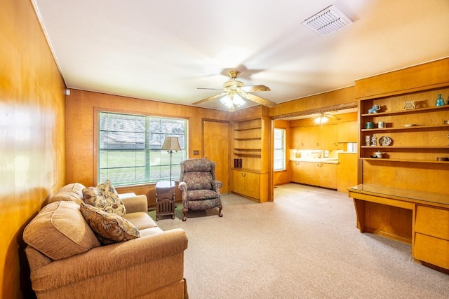 sitting room featuring visible vents, a ceiling fan, light colored carpet, built in study area, and wood walls