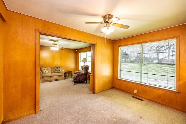 living room with light carpet, wood walls, visible vents, and a wealth of natural light