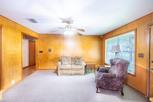 living room with ceiling fan, wooden walls, visible vents, and light colored carpet