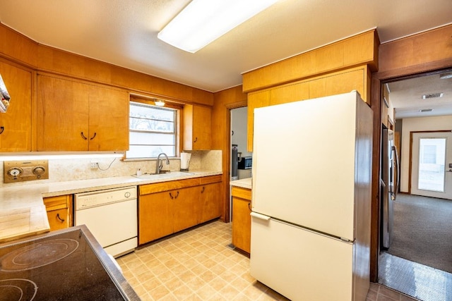 kitchen featuring brown cabinets, white appliances, light countertops, and a sink