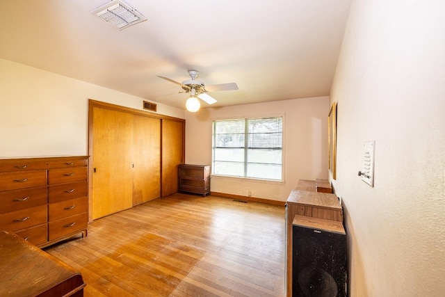 bedroom with light wood-style floors, a ceiling fan, visible vents, and a closet