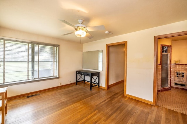 empty room featuring baseboards, visible vents, ceiling fan, wood finished floors, and heating unit