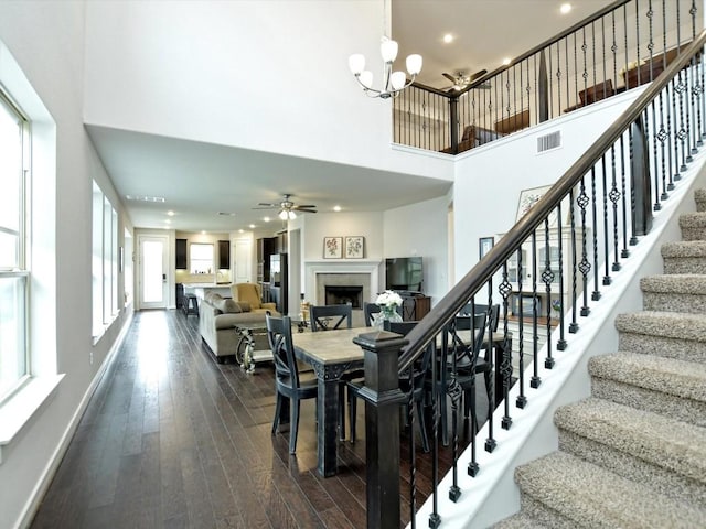 dining room featuring a high ceiling, a fireplace, visible vents, stairway, and dark wood finished floors