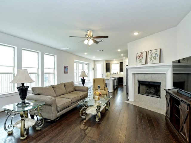 living room with ceiling fan, a tiled fireplace, dark wood-type flooring, and recessed lighting